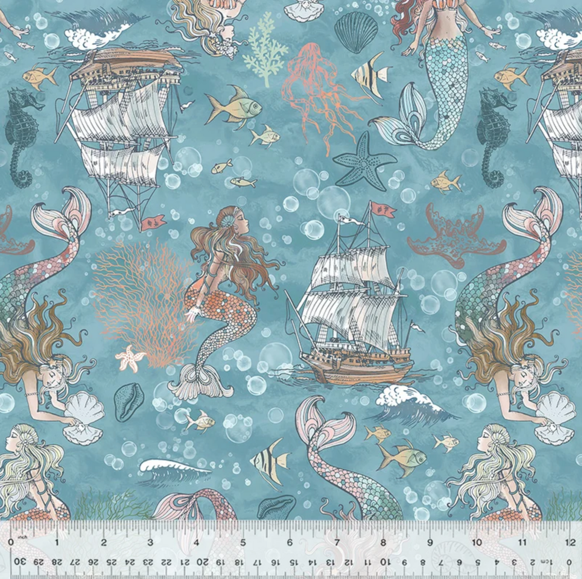 A close-up of a fabric pattern featuring mermaids, sailboats, starfish, bubbles, and sea life on a teal-blue background, with a ruler along the bottom edge showing scale.