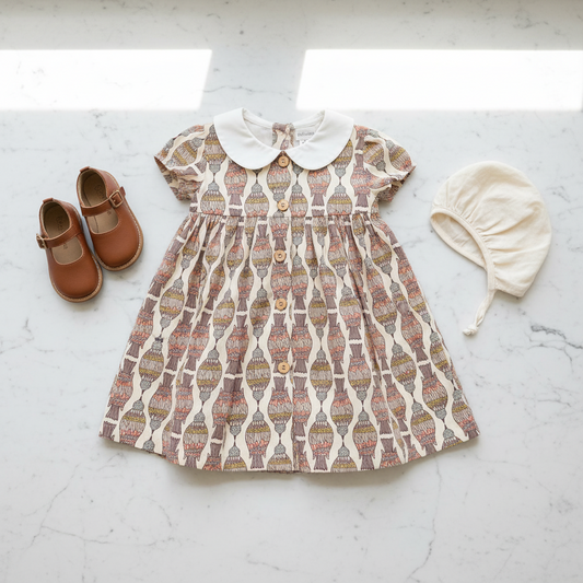 Children's patterned dress with shoes and bonnet on a light surface
