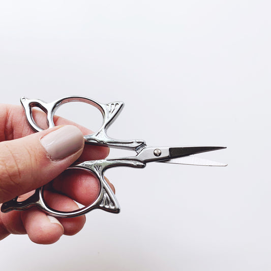Hand holding a pair of silver scissors against a white background