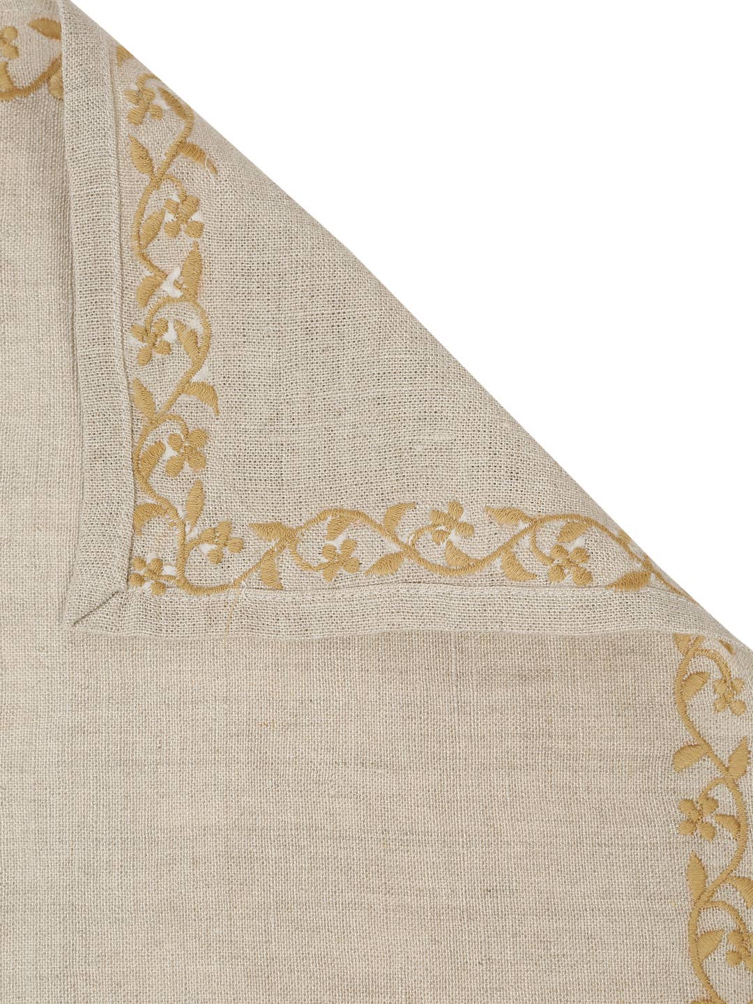 A close-up of a beige woven napkin, folded to show its corner with a gold floral vine border pattern on a white background.