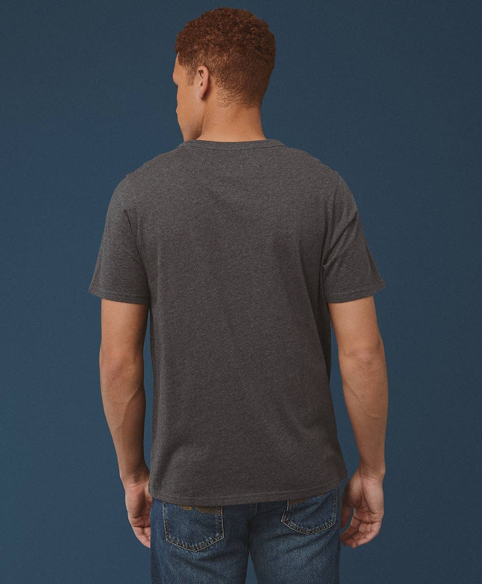 Man wearing a dark gray t-shirt and blue jeans against a navy background