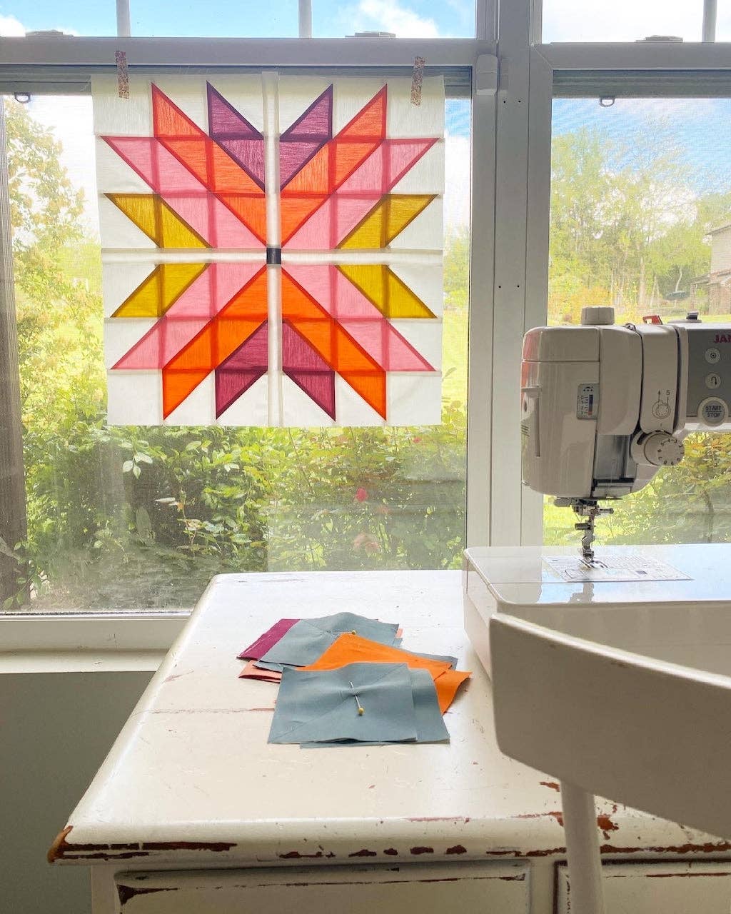 Quilt with star pattern on a window, sewing machine on a table with fabric