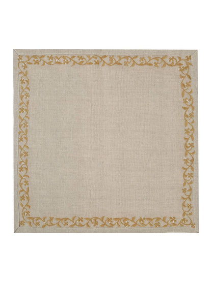 The backside of a square beige napkin with a textured linen-like surface and a decorative border featuring a repeating gold floral and vine pattern, shown flat against a white background.