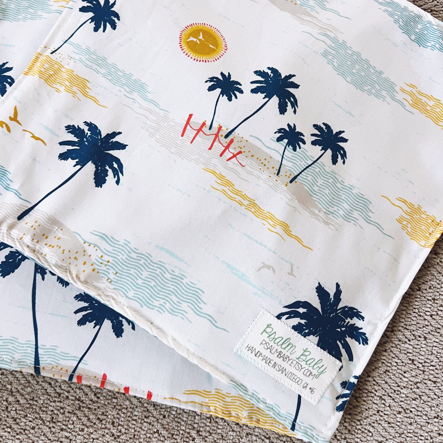 Folded fabric with palm tree and beach design, featuring a brand label.