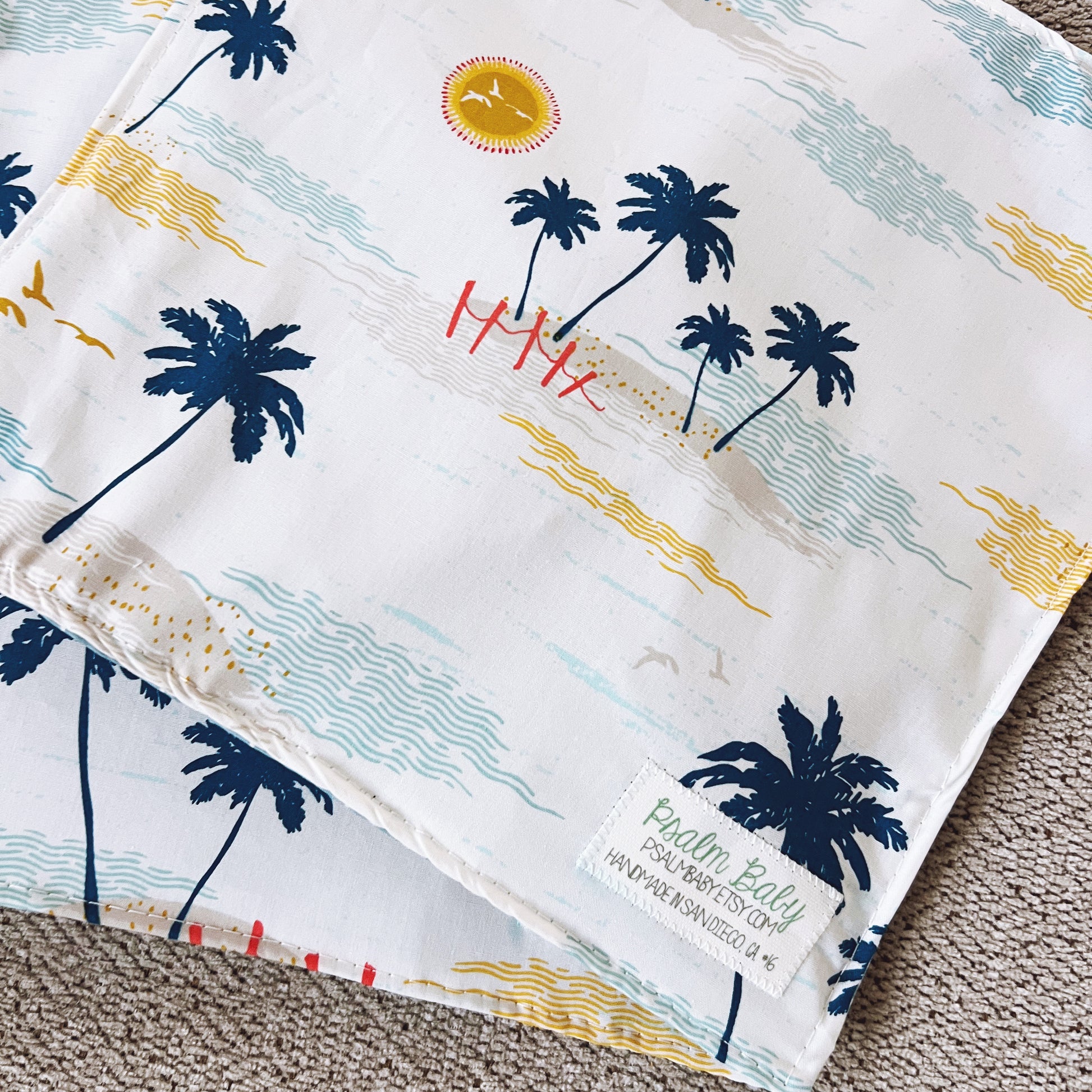 Folded fabric with palm tree and beach design, featuring a brand label.