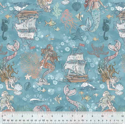 A close-up of a fabric pattern featuring mermaids, sailboats, starfish, bubbles, and sea life on a teal-blue background, with a ruler along the bottom edge showing scale.