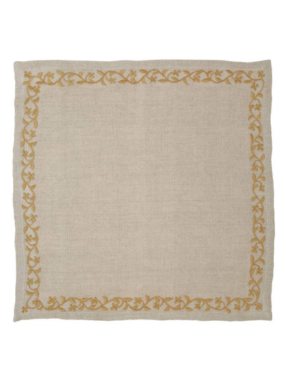 A square beige linen napkin featuring a decorative border of gold floral and vine patterns along all four edges, shown flat against a white background.