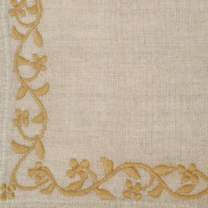 Close-up of a beige linen fabric napkin with a decorative border of gold floral vines along the left and bottom edges.