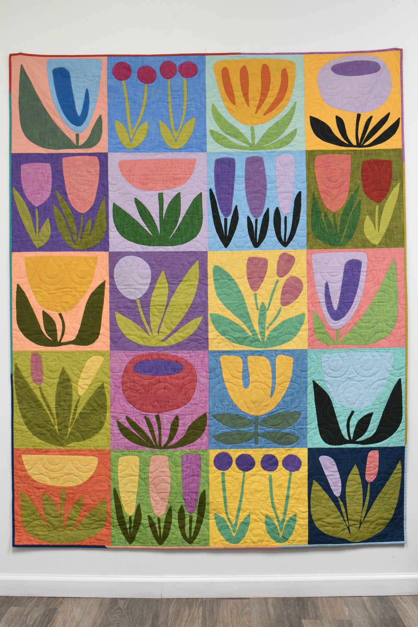 Colorful quilt with geometric floral patterns on a white wall.
